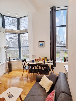 A modern living room with a dining area, large windows, and a view of a tall building. - Urban Stay Shard View Apartments (London)