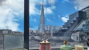 A window view of a modern cityscape with a prominent skyscraper, a clear sky, and a table with decorative items. - Urban Stay Shard View Apartments (London)