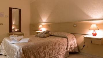 A hotel room with a bed, two bedside lamps, a nightstand, a mirror, and a wall-mounted thermostat.