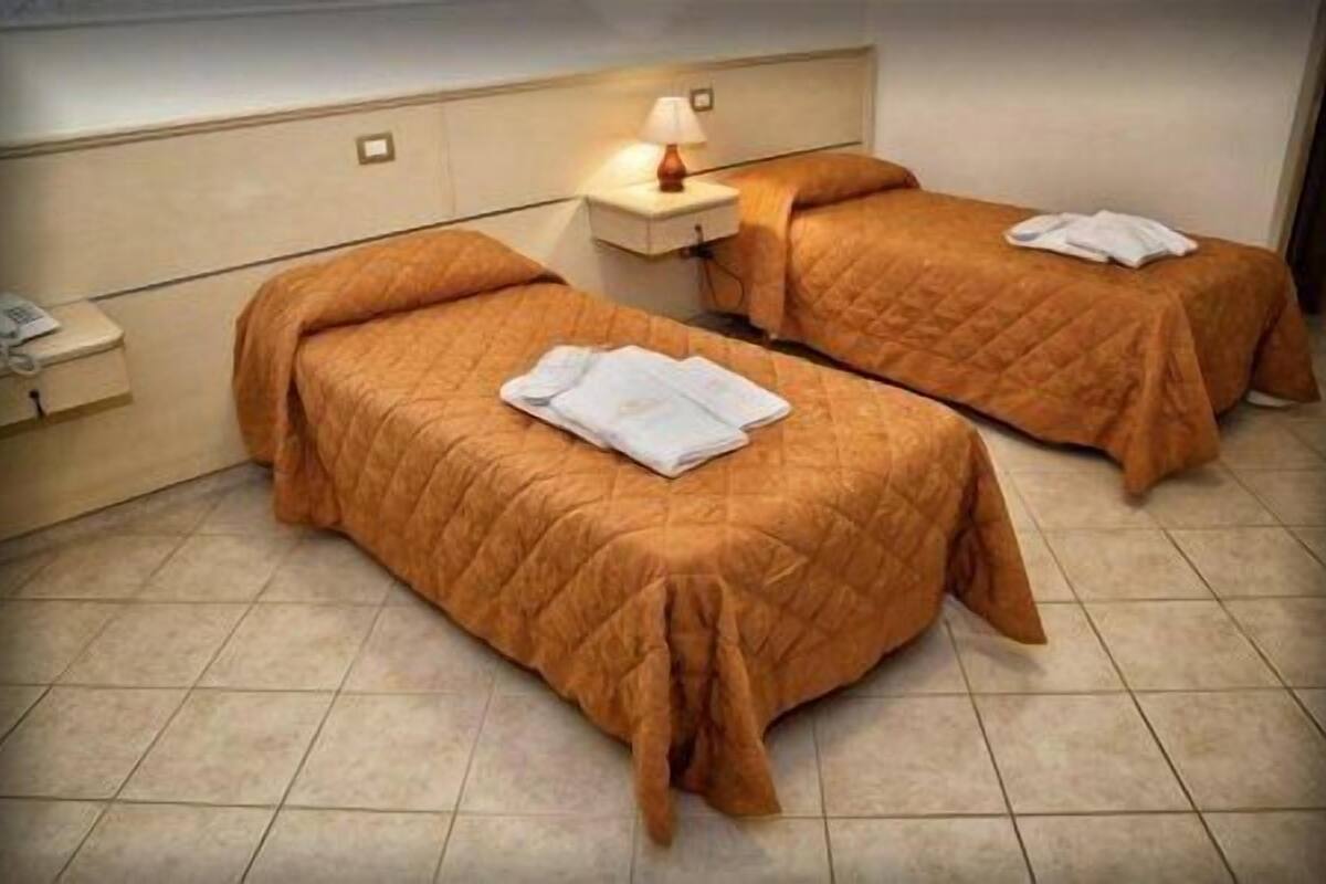 A hotel room with two beds, each with a duvet and a folded towel. There is a bedside table with a lamp and a phone.