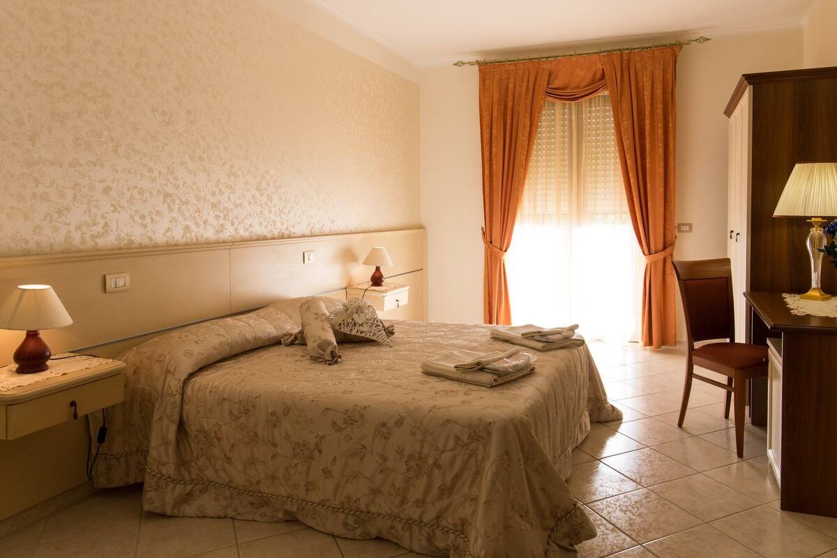 A hotel room with a bed, two bedside lamps, a desk with a lamp, and a chair.