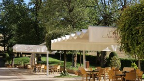 An outdoor seating area with tables and chairs under a canopy, surrounded by greenery and trees. - Elia Hotel (Buccino)