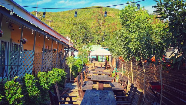 An outdoor seating area with tables and chairs, surrounded by greenery and a building with a red roof. - Felice Resort (Koh Lan)