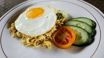 A plate of noodles topped with a fried egg, accompanied by slices of cucumber and tomato.