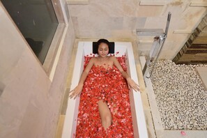 A bathtub filled with red rose petals, a showerhead, and a tiled floor. - Bali Taman Sari Villa & Restaurant (Negara)