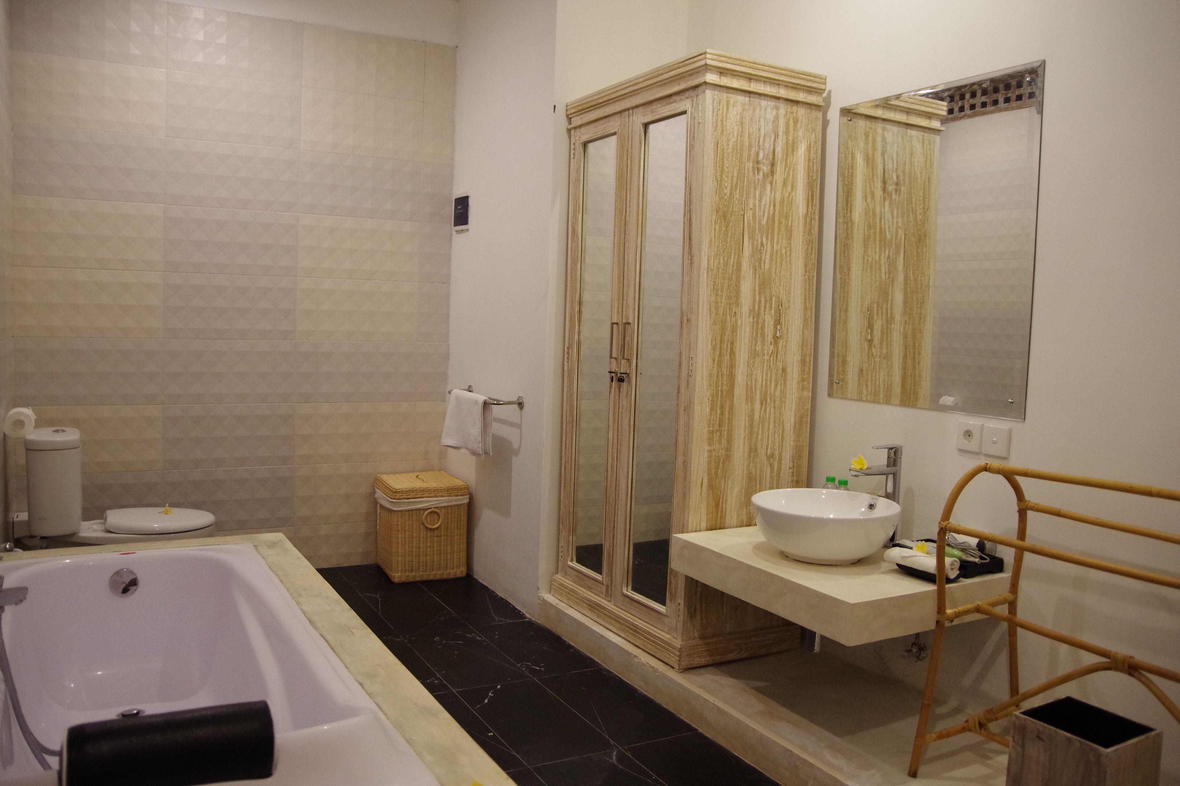 Un baño con bañera, un armario de madera con espejo, un lavabo y una pequeña cesta de mimbre.