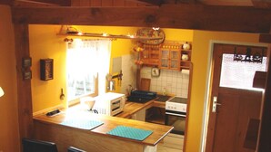 Cocina con armarios de madera, un microondas y una estufa. Hay dos taburetes negros y un ventanal con cortinas.