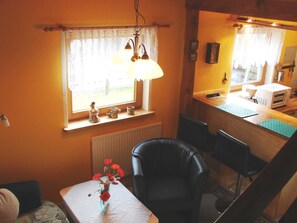 Eine kleine Küche mit einem Fenster, einem Tisch mit Blumen in einer Vase und einem Stuhl.