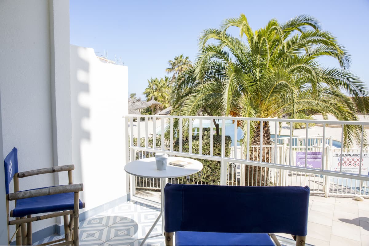 Un balcon avec deux chaises, une petite table et une vue sur des palmiers et une piscine.