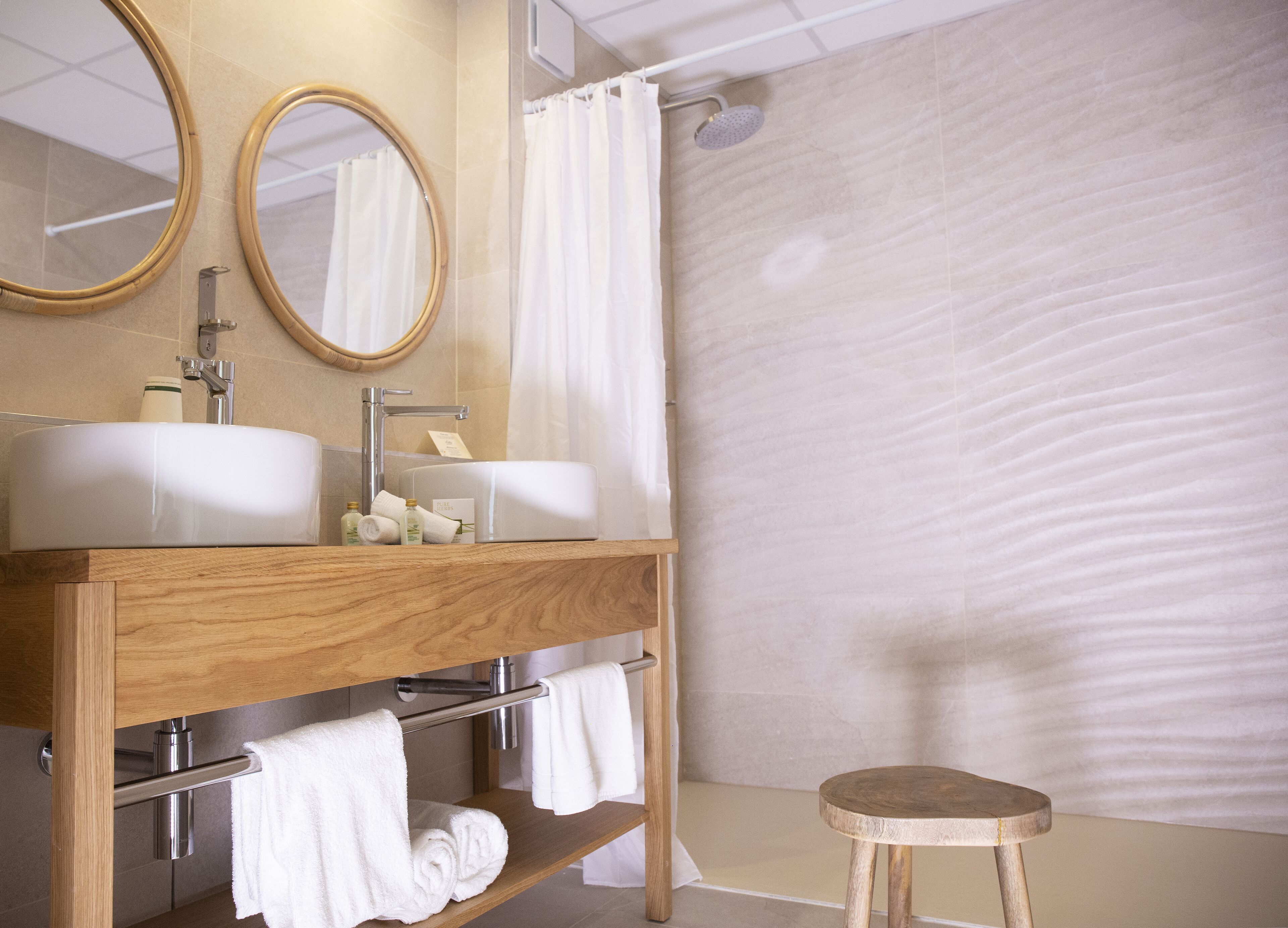 A bathroom with two sinks, a mirror, a shower curtain, and a wooden stool.