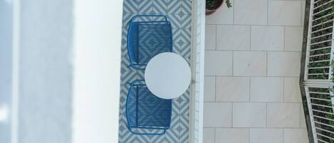 A patio with a white round table and two blue chairs, a potted plant, and a patterned floor.