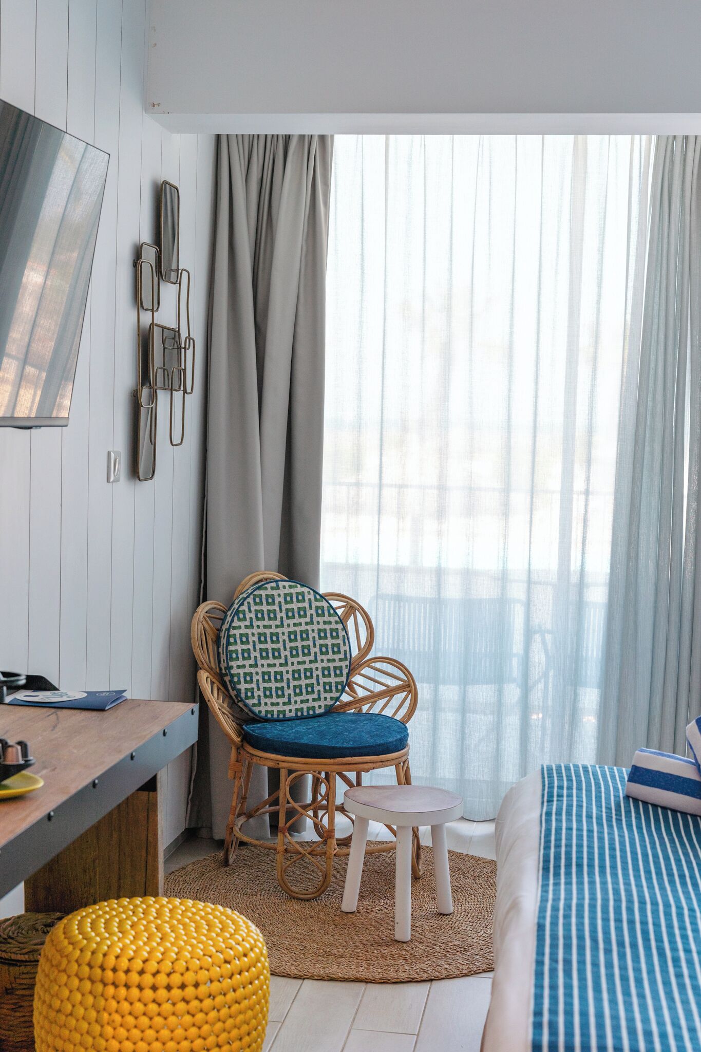 Une pièce comprenant un lit, une chaise avec un coussin à motifs, une petite table et un pouf jaune.