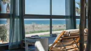 Una habitación con un ventanal grande que da a una playa, una mesa de madera y una silla.