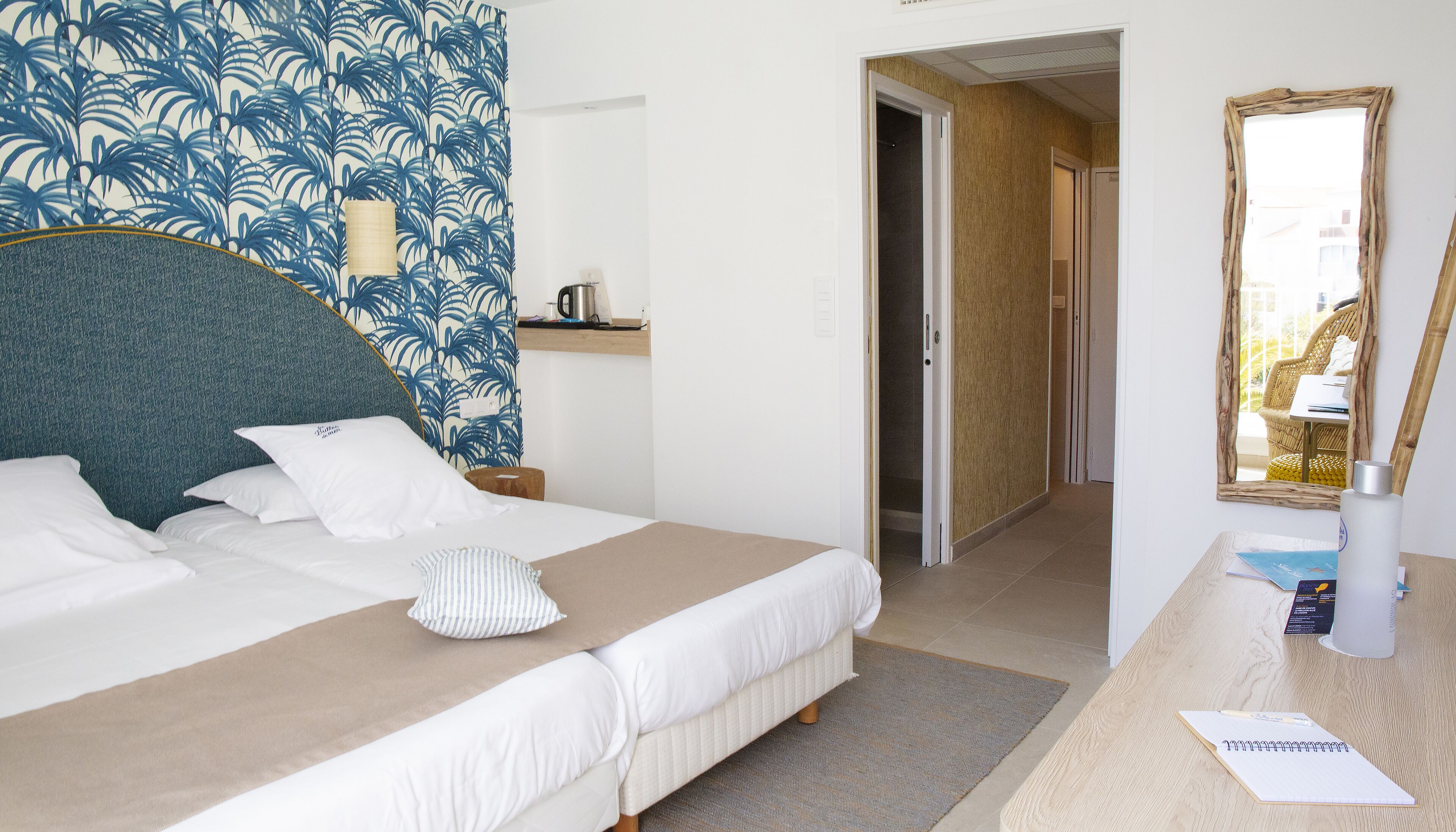 Habitación de hotel con una cama grande, una mesita de noche con lámpara, un espejo y vistas al exterior.