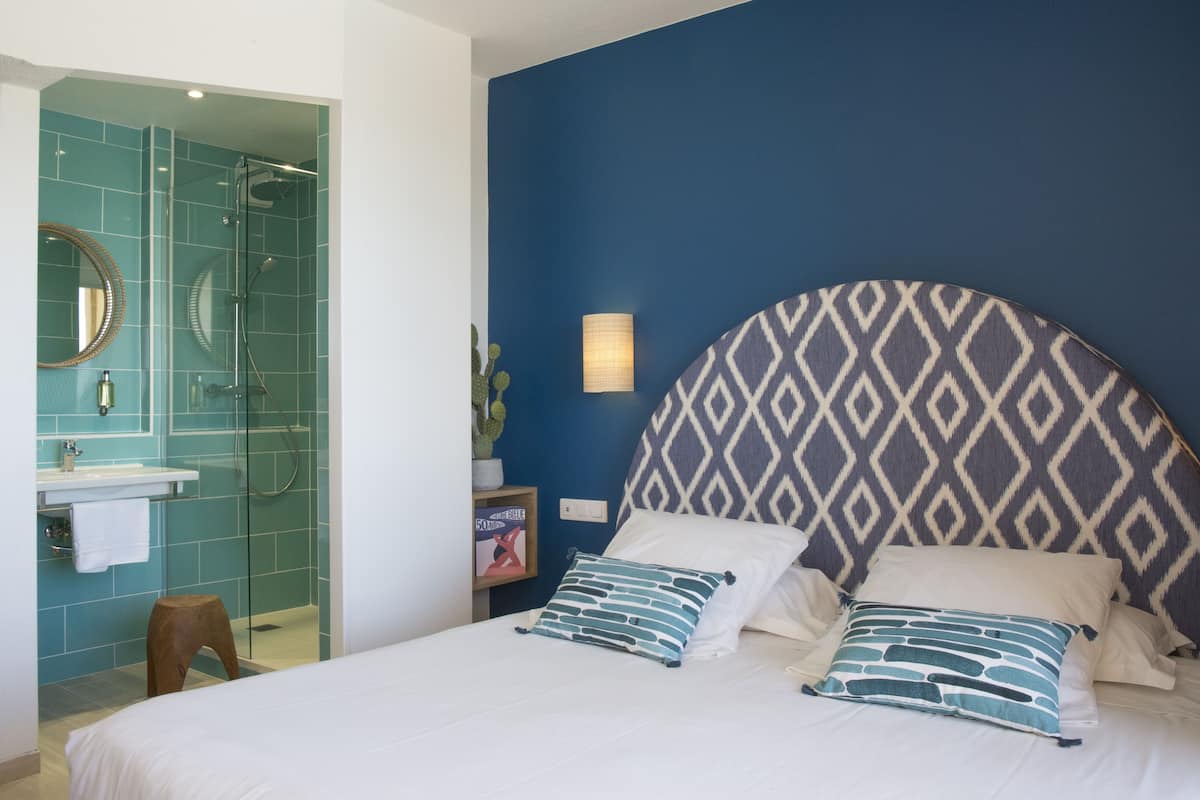 Une chambre à coucher avec un grand lit, une tête de lit ornée d’un motif géométrique et une table de chevet avec une lampe.