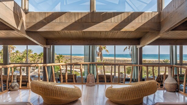 Terraza de madera con mobiliario de mimbre con vista a la playa.