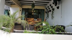 Un espace de restauration en plein air avec des tables et des chaises en bois, entouré de plantes en pot et d’une plante suspendue.
