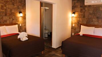 Habitación de hotel con dos camas, una pared de piedra, piso de madera y un baño visible a través de una puerta abierta.