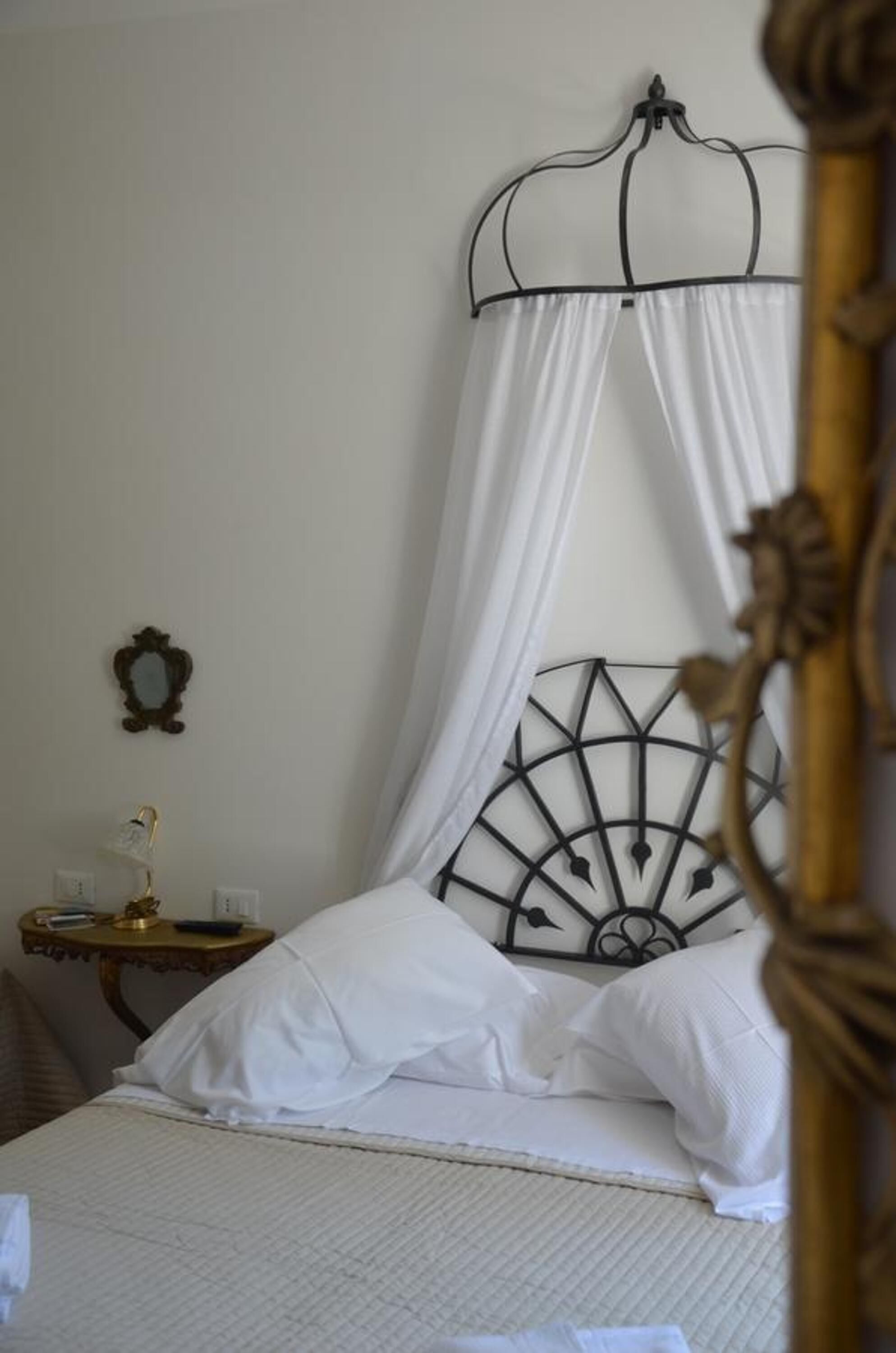 Ein Bett mit Baldachin, ein Nachttisch mit Lampe und ein dekorativer Spiegel an der Wand.