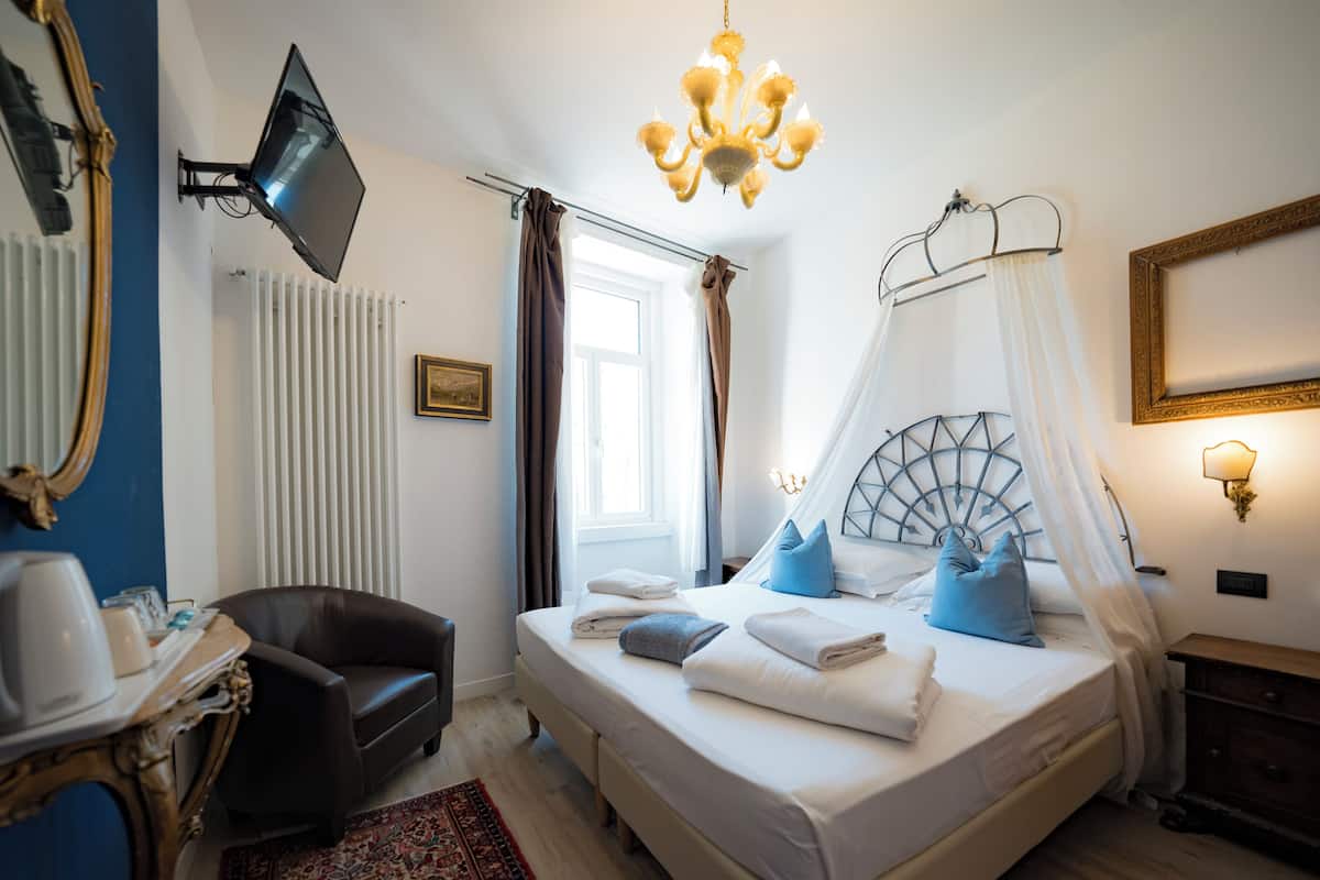 A bedroom with a bed, a chair, a television, a chandelier, a bedside table, and a nightstand.