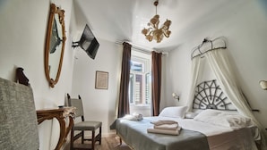 A bedroom with a bed, a chair, a desk, a mirror, a television, and a window with curtains. - La Loggia del Castello (Trento)