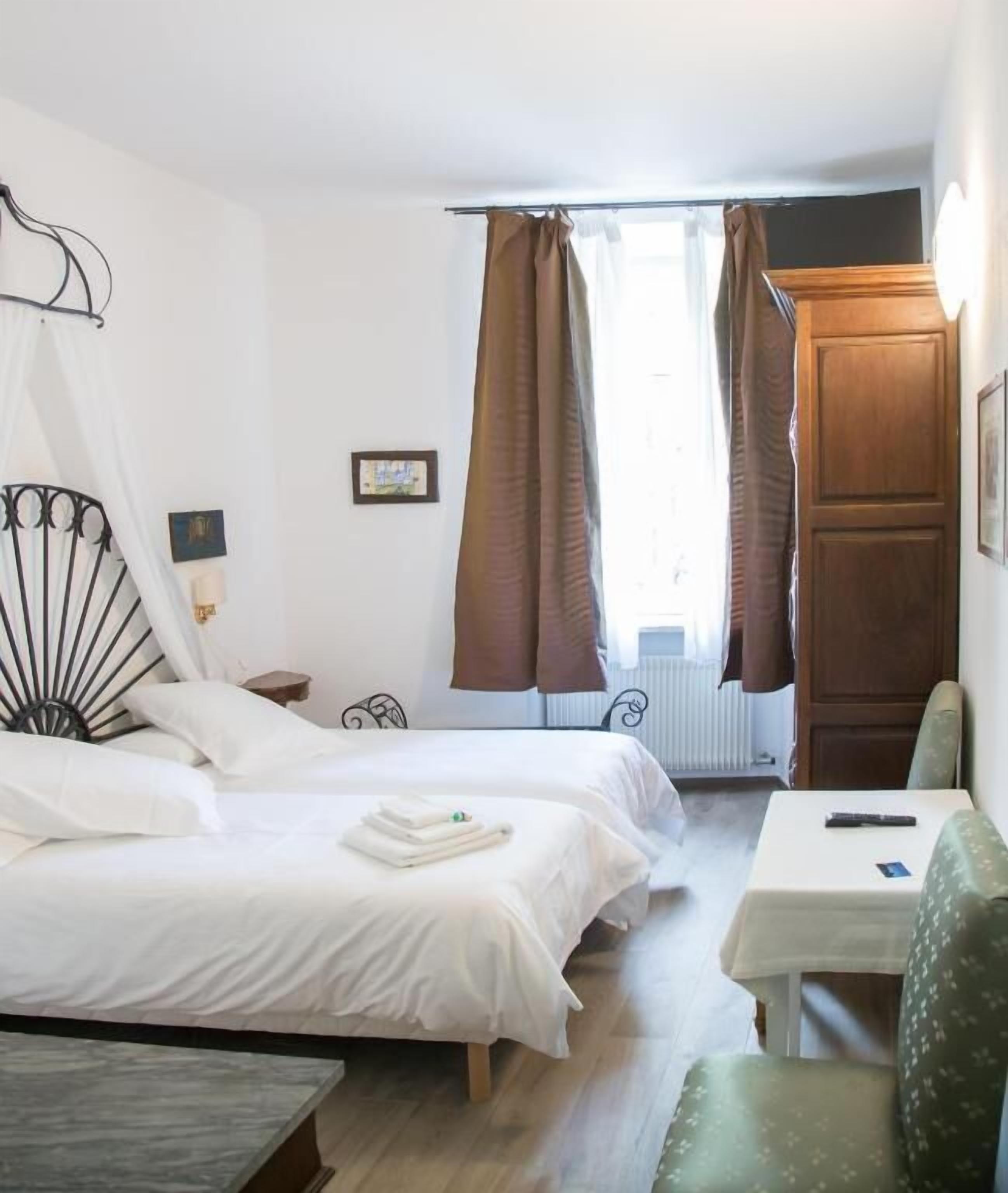 Une chambre d’hôtel avec deux lits, une petite table, une chaise et une fenêtre avec des rideaux.