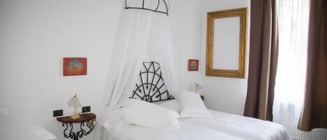 Un dormitorio con cama a dosel, mesita de noche con lámpara, espejo y alfombra roja.