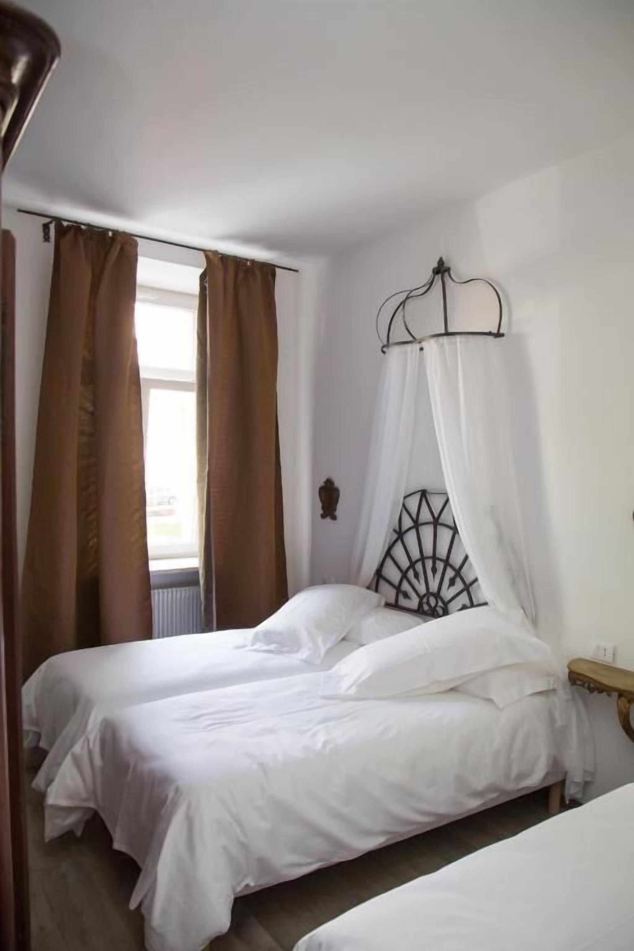 A bedroom with two single beds, a window with brown curtains, and a canopy bed with a metal headboard.