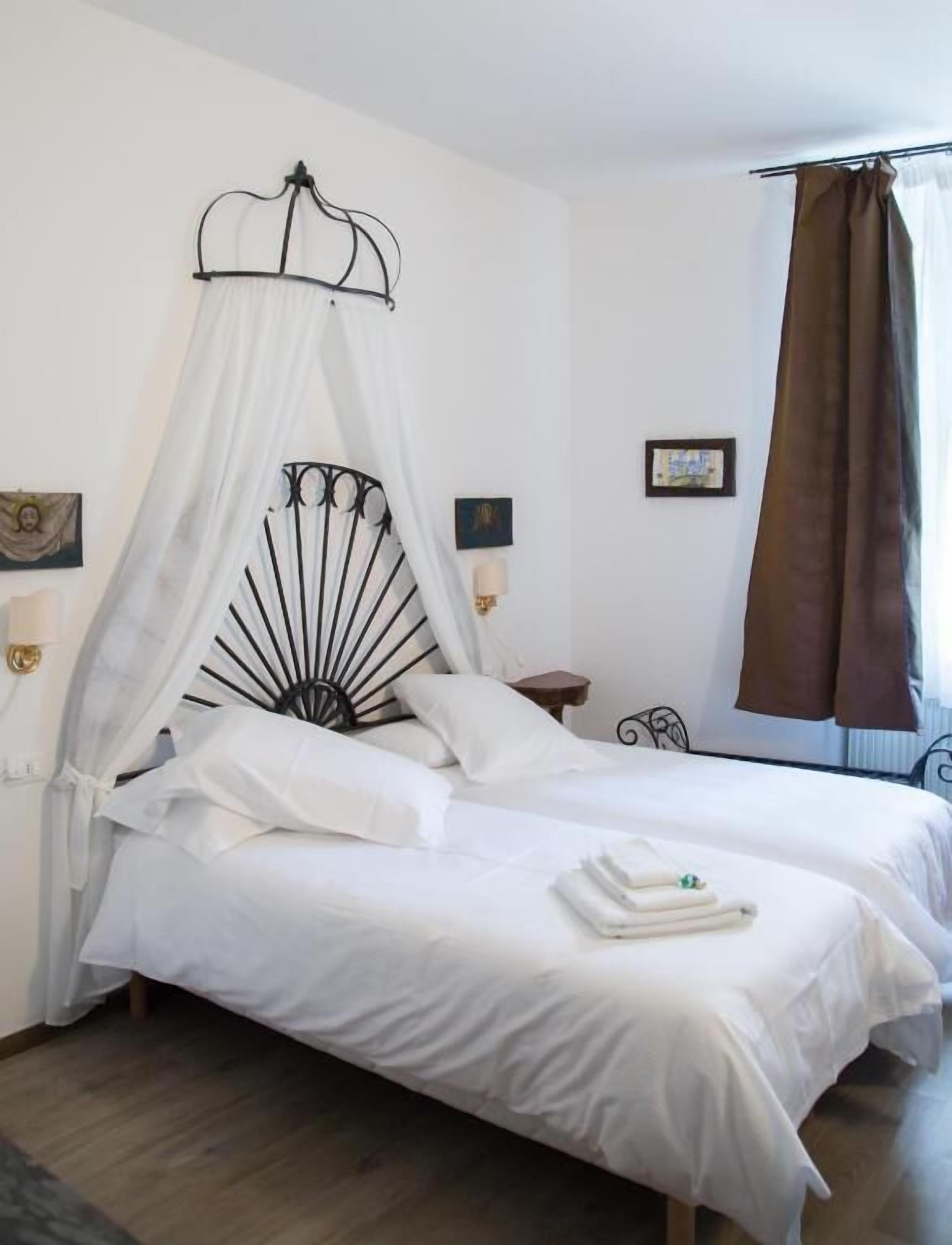 Cama doble con dosel, dos mesitas de noche y una ventana con cortinas.