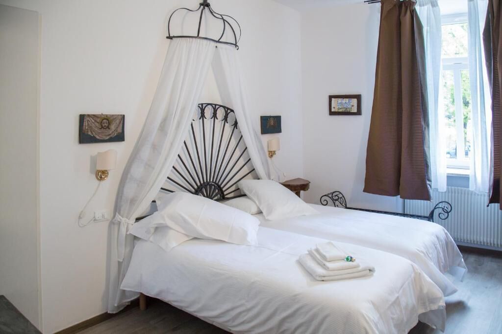 A bedroom with two beds, a canopy bed, bedside lamps, a window with curtains, and framed pictures on the wall.