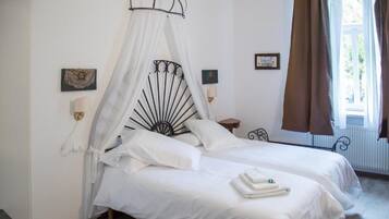 A bedroom with two beds, a canopy bed, bedside lamps, a window with curtains, and framed pictures on the wall.