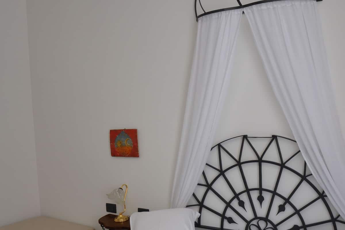 A hotel room with two beds, a nightstand with a lamp, a decorative headboard, and a small painting on the wall.