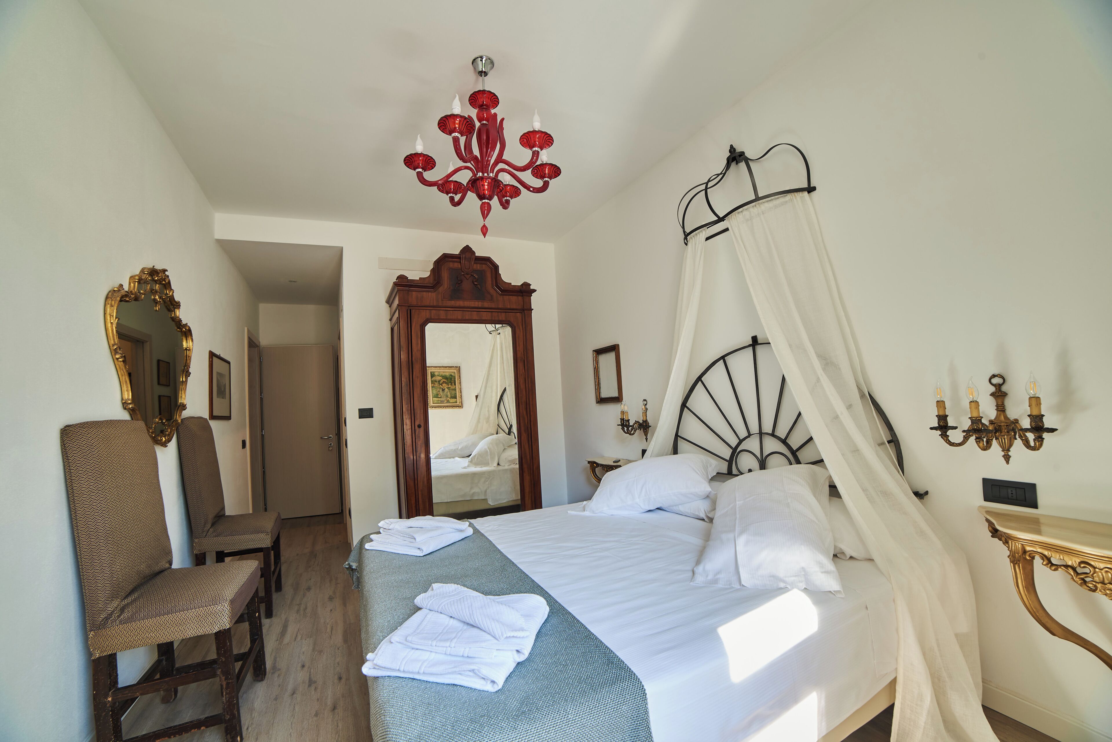 A bedroom with a bed, a canopy, a chandelier, a mirror, and a chair.