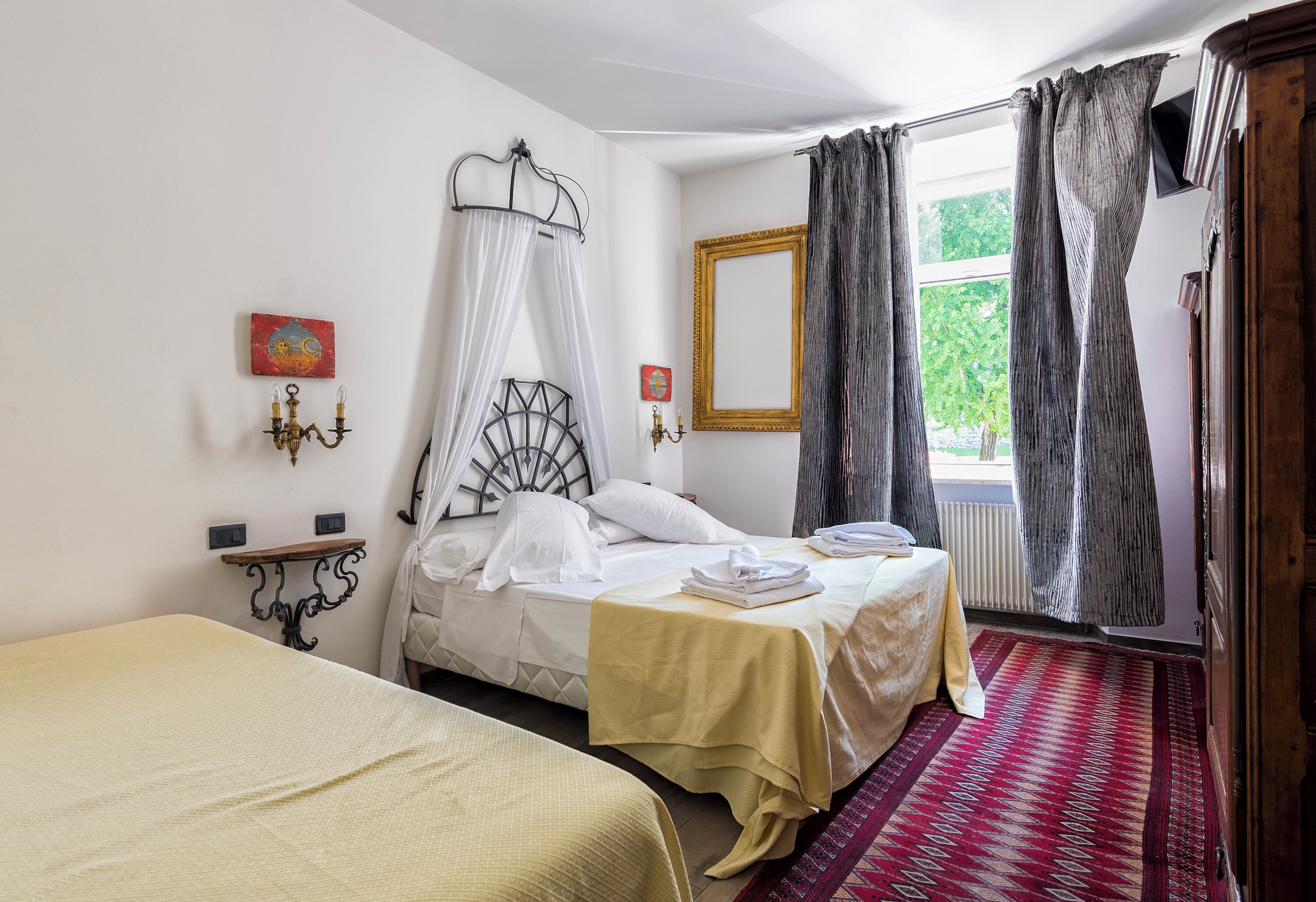 A bedroom with two beds, a window with curtains, a radiator, and a wall-mounted artwork.