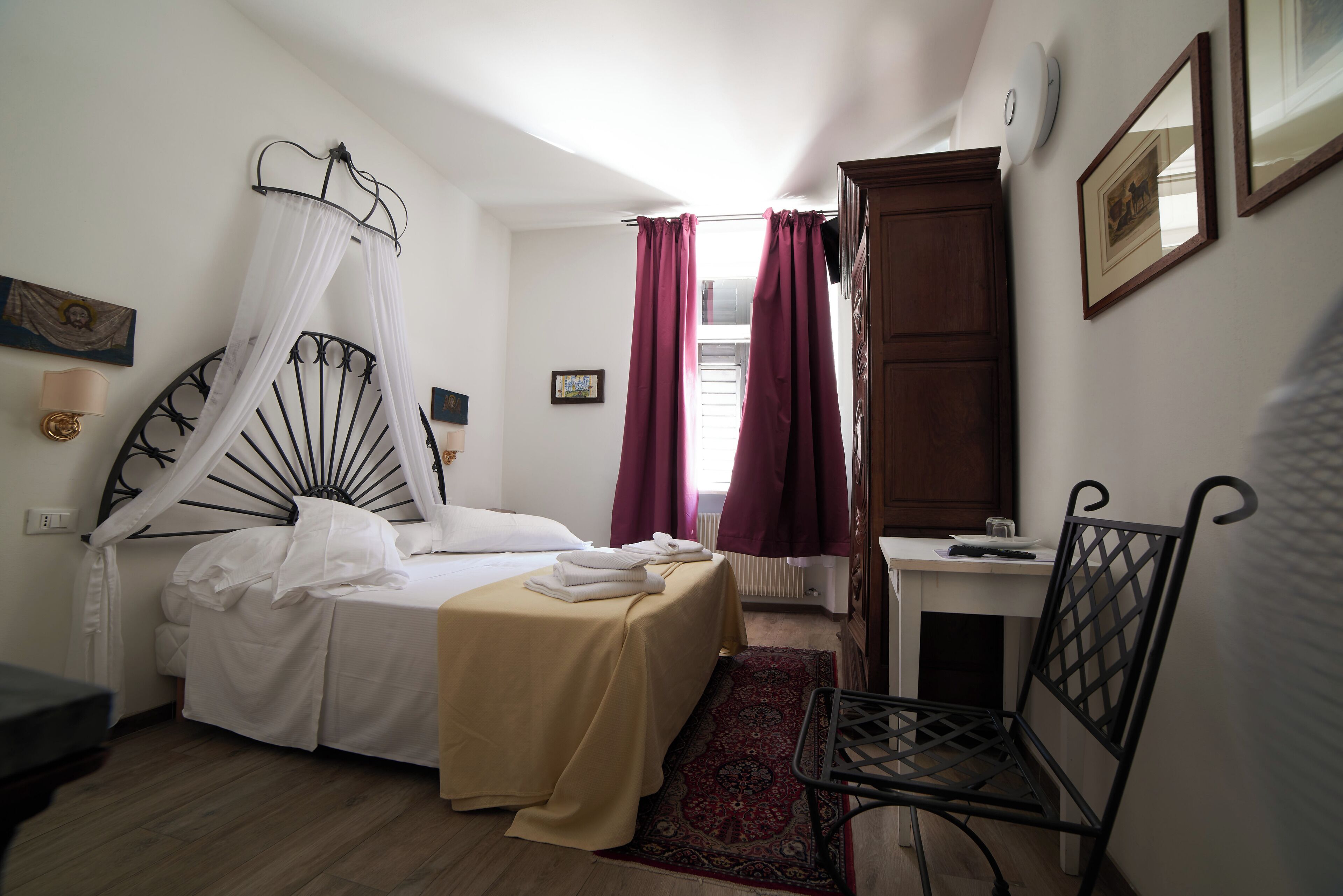 A bedroom with a bed, a chair, a desk, and a window with curtains.