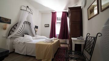 A bedroom with a bed, a chair, a desk, and a window with curtains.