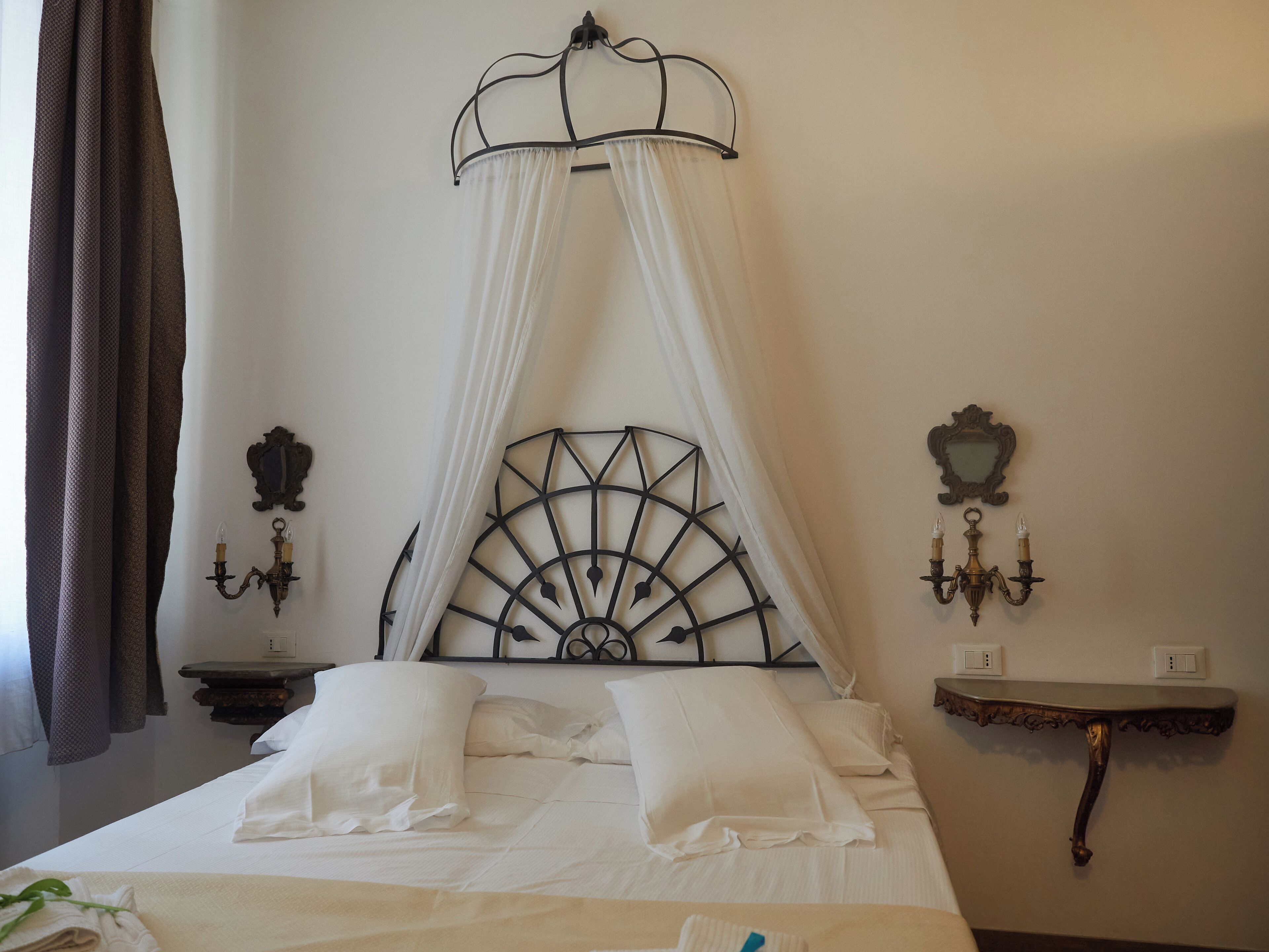 Une chambre à coucher avec un lit à baldaquin, deux appliques murales, une petite table et une étagère fixée au mur.