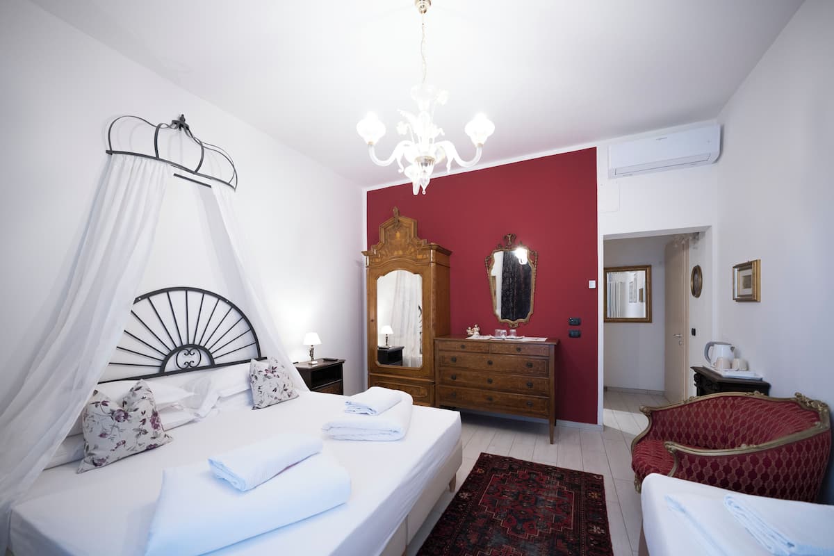 A bedroom with a bed, bedside table, mirror, dresser, and a red wall.