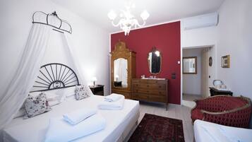 A bedroom with a bed, bedside table, mirror, dresser, and a red wall.