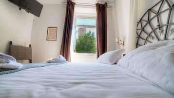 A hotel room with a bed, a TV mounted on the wall, a window with curtains, and a framed picture on the wall.