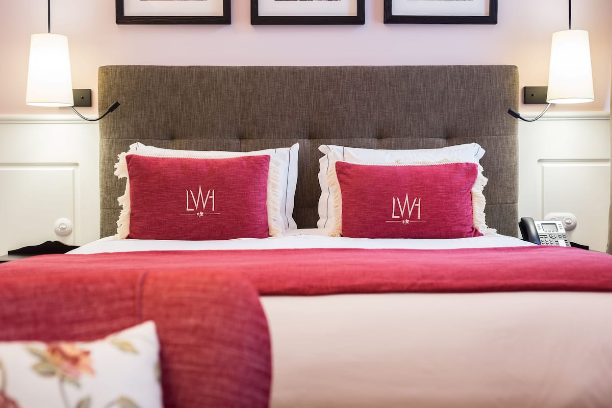 Ein Hotelzimmer mit einem großen Bett, zwei Kissen mit bestickten Initialen, Nachttischlampen und einem Telefon auf dem Nachttisch.