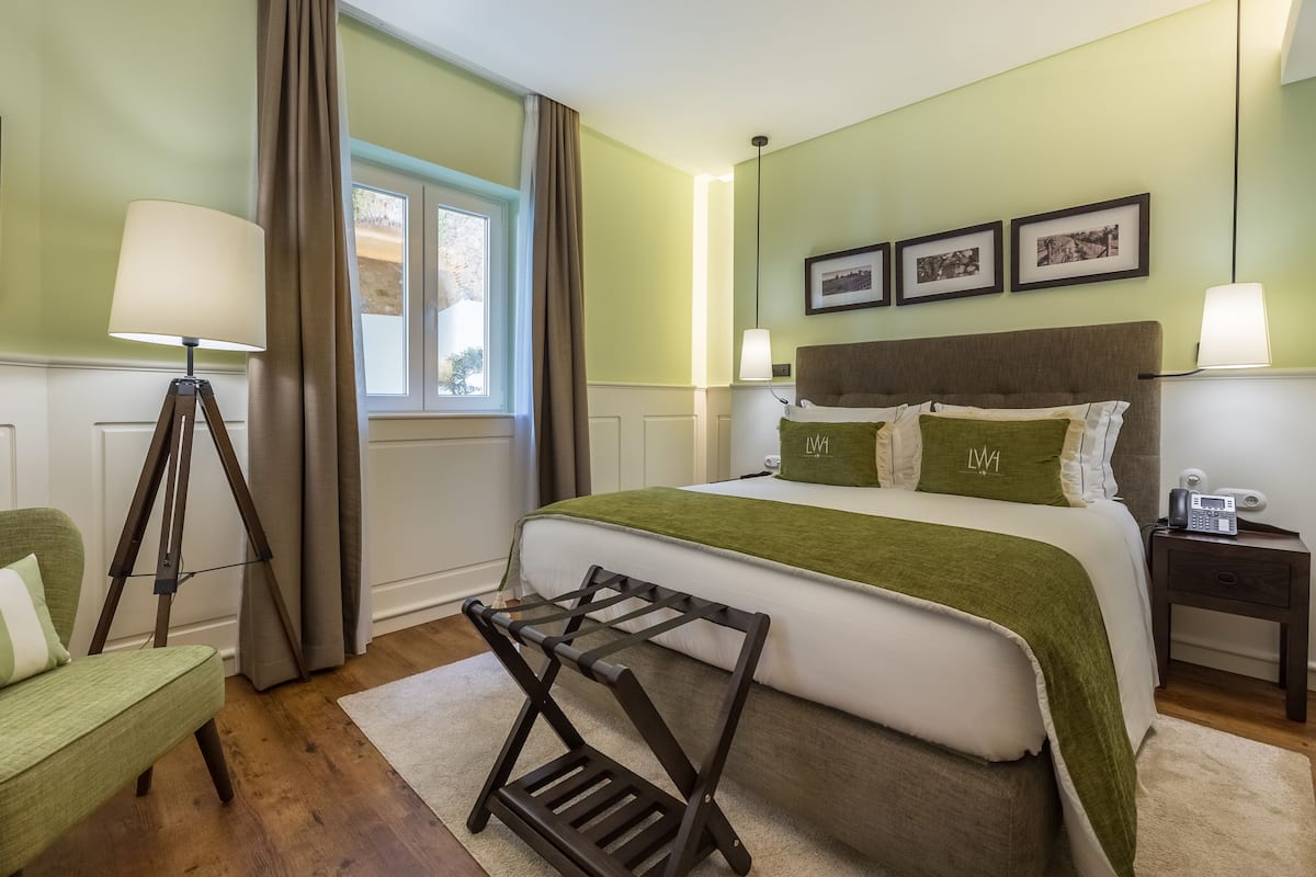 Ein Schlafzimmer mit einem Bett, einem Nachttisch, einer Lampe, einem Sessel und einem Fenster mit Vorhängen.