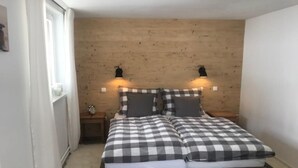 A bedroom with a wooden headboard, two bedside tables, a checkered bedspread, and two wall-mounted lamps. - Kraeuterhof-Ferienwohnung (Missen-Wilhams)
