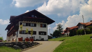 A two-story building with a sloped roof, large windows, and a pathway leading to the entrance. - Kraeuterhof-Ferienwohnung (Missen-Wilhams)