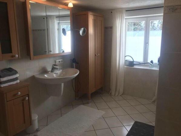 Un baño con lavamanos, espejo, armario de madera y ventana con cortinas.