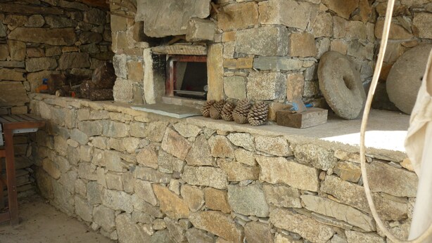 A stone-walled interior with a fireplace, wooden beams, and a rustic bench.