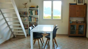A room with a white table and chairs, a bookshelf, a wooden cabinet, and a window with a view of trees.