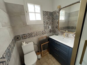 Une salle de bain avec des carreaux décorés, des toilettes, un lavabo avec un miroir et une petite fenêtre.