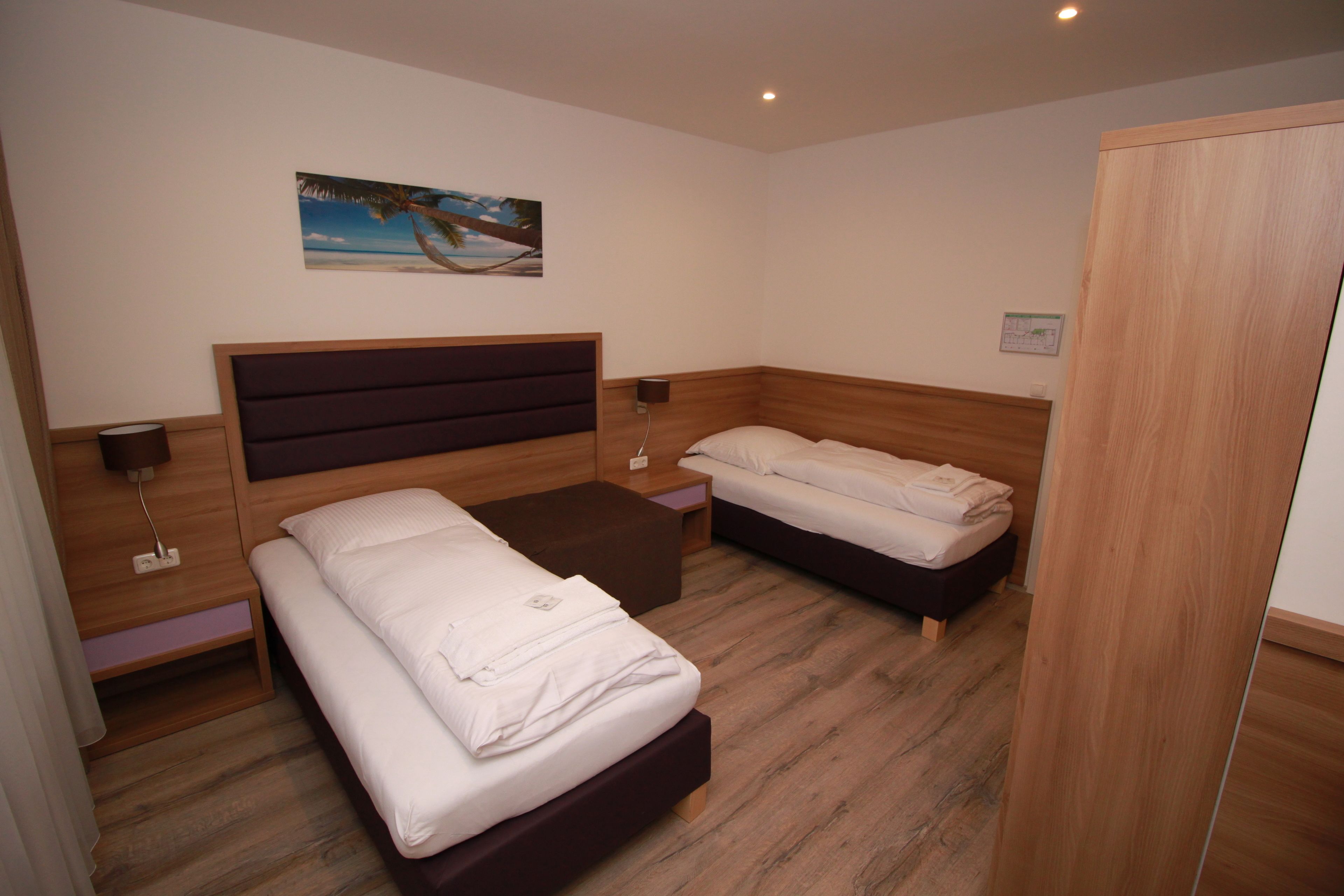 Une chambre avec deux lits, des têtes de lit en bois, une table de chevet avec une lampe et un tableau au mur.
