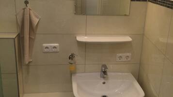A bathroom with a sink, mirror, towel rack, and a wall-mounted light fixture.